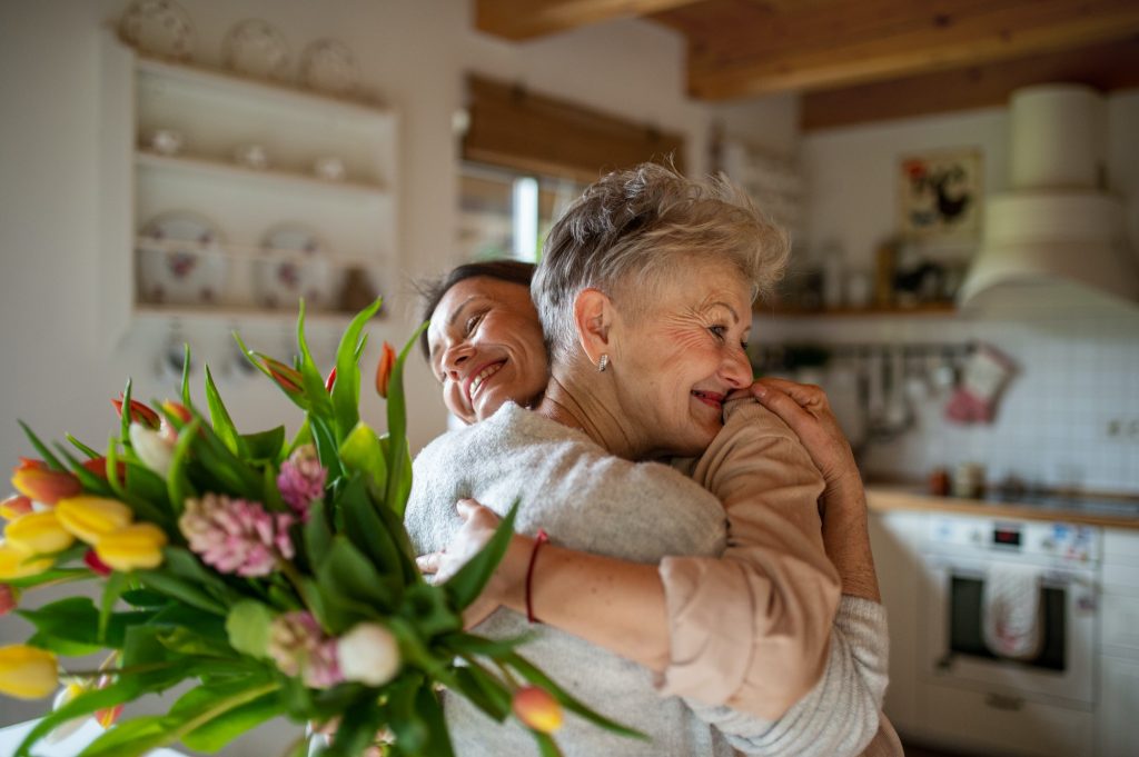 Happy senior mother hugging adult daughter indoors at home, mothers day